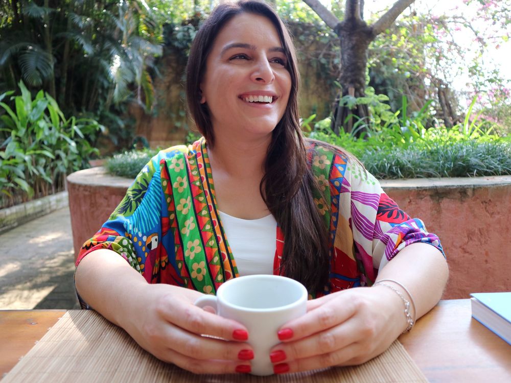 Janaína Morelli sorrindo, com uma xícara nas mãos, em um jardim